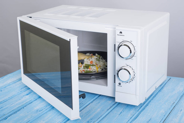 forno de microondas branco, sobre uma superfície de madeira azul para aquecimento de alimentos
 - Foto, Imagem