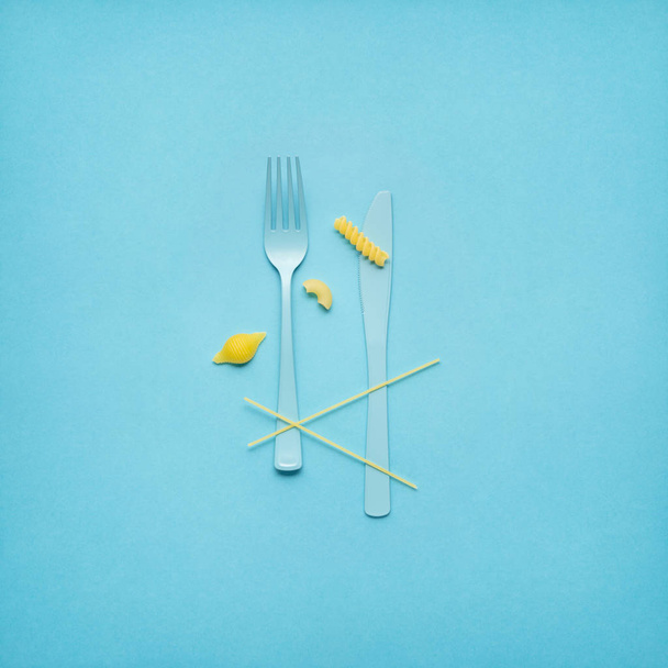 Tasty pasta. Creative still life photo of fork and spoon with raw pasta on blue background. - Foto, Imagem