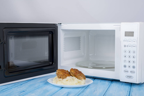 λευκό φούρνο μικροκυμάτων, σε μια μπλε ξύλινη επιφάνεια για τη θέρμανση τροφίμων - Φωτογραφία, εικόνα