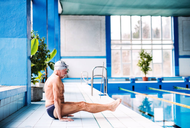 Senior man stretching by the indoor swimming pool. - Photo, Image