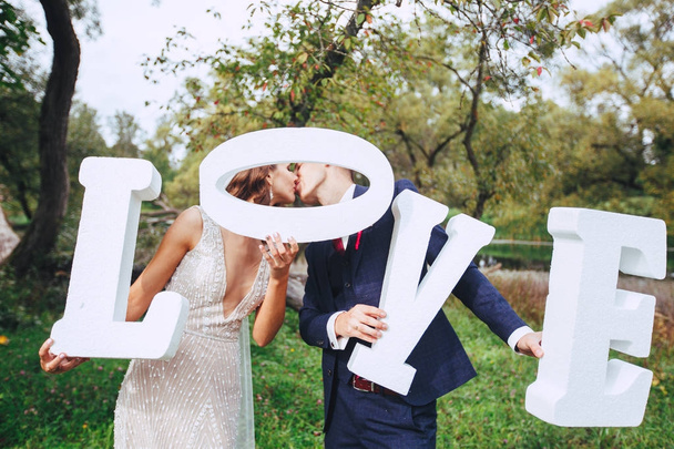 Happy wedding couple holding big white love letters and kissing - Fotoğraf, Görsel