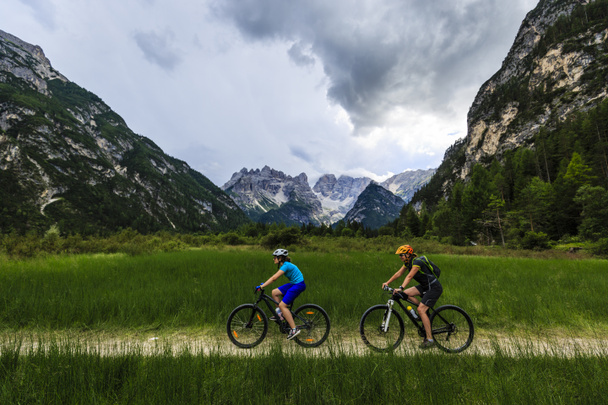 Mountain biking woman and young girl along river in Dolomites, I - Photo, Image