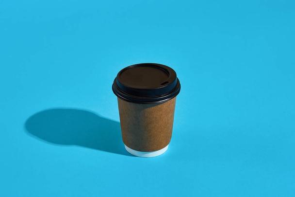 Warme koffie in bruin papier beker met zwarte deksel op blauwe achtergrond - Foto, afbeelding