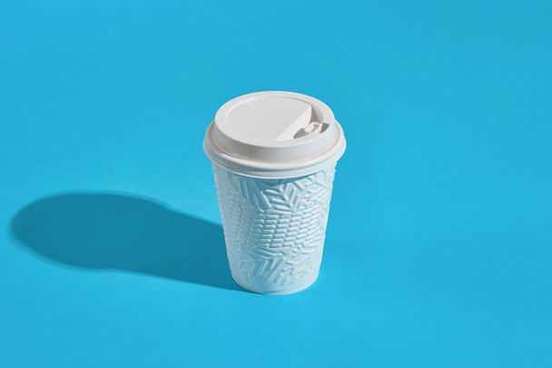 Warme koffie in witte winter papier beker met deksel op blauwe achtergrond - Foto, afbeelding