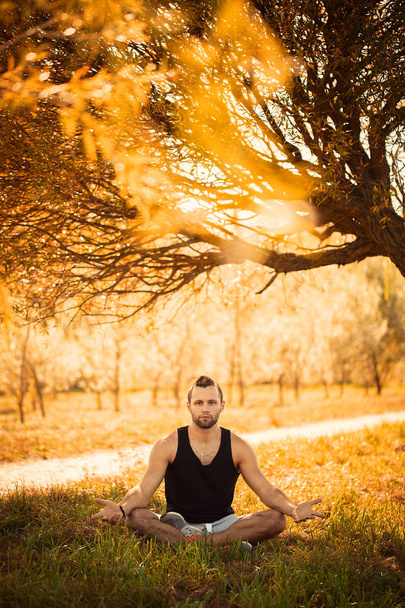 Йога и концепция здорового образа жизни. Портрет человека, медитирующего в удобной позе на траве в парке. Яркая вспышка теплого тонуса
 - Фото, изображение