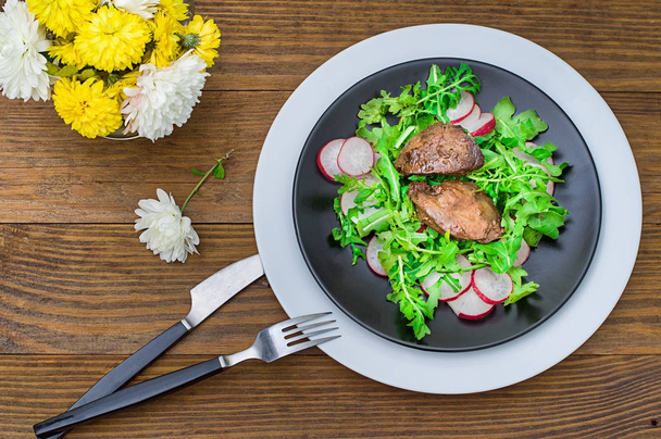 鶏レバー、ルッコラ添え黒皿に大根と温かいサラダ。木製の素朴な背景。選択と集中。トップ ビュー - 写真・画像