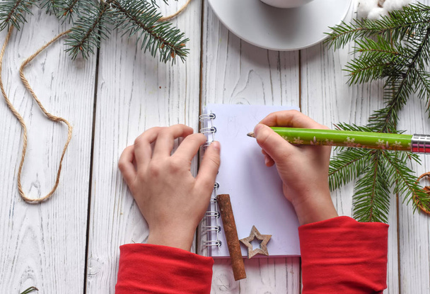 A festive photo of children`s hands writing in a note book, a cuo of tea anf Christmas decoration - Foto, imagen