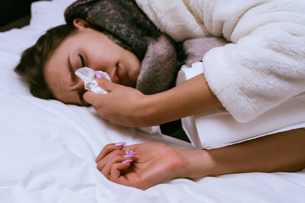sad young girl gets sick, sneezes, lies in bed - Fotó, kép