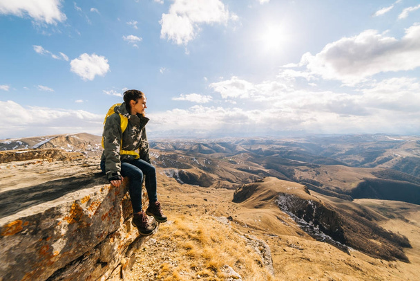 young woman traveler sits on the edge of the cliff, enjoys nature and the sun - Foto, imagen