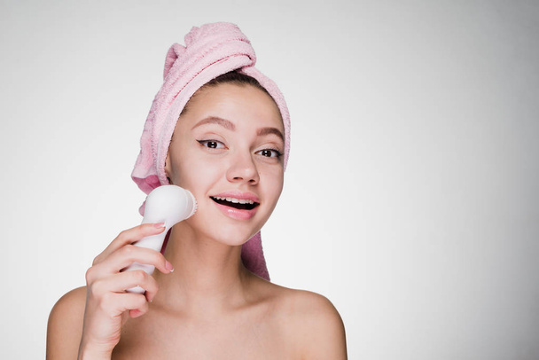 happy smiling woman with pink towel on head cleans face with electric brush - Photo, image