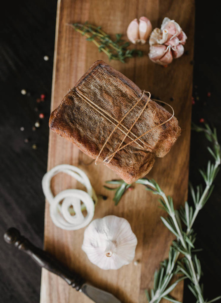 Chunk of salted smoked lard in gauze with a rope.Traditional Russian and Ukrainian meal.Healthy food with spices, herbs, onion and garlic.Food photo for recipe or cookbook. Rustic clolor style - Fotografie, Obrázek