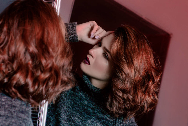 Портрет плача возле зеркала красивый нежный кудрявый грустно расстроен депрессивный одинокая женщина в сером свитере в темной комнате
 - Фото, изображение
