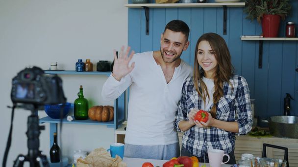 Cheerful attractive couple recording video food blog about cooking on dslr camera in the kitchen at home - Φωτογραφία, εικόνα