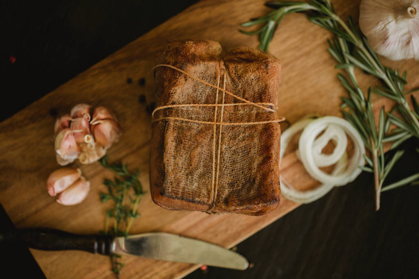 Chunk of salted smoked lard in gauze with a rope.Traditional Russian and Ukrainian meal.Healthy food with spices, herbs, onion and garlic.Food photo for recipe or cookbook. Rustic clolor style - Foto, afbeelding