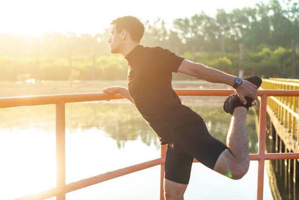 Ο άνθρωπος γυμναστικής τεντώνοντας το πόδι του πριν ένα τρέξιμο σε εξωτερικούς χώρους. - Φωτογραφία, εικόνα