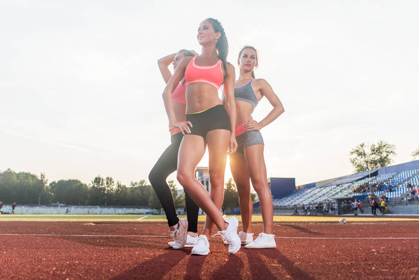 Group of fit young sportswomen standing on athletics stadium and posing. - Фото, изображение