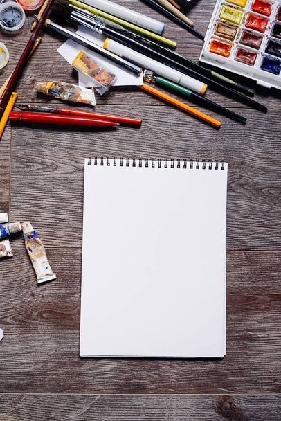 on a wooden surface is a white notepad for drawing, artistic paints and brushes - 写真・画像
