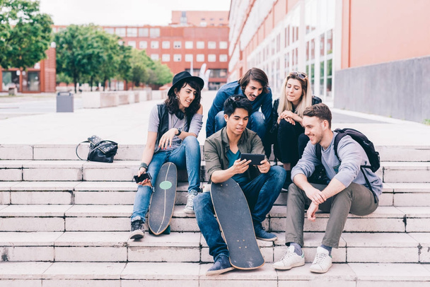 Group of friends multiethnic sitting outdoor using smartphone - 写真・画像
