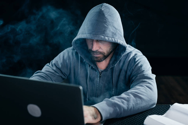 mysterious bearded man hacking does something illegal on a laptop, in the dark - Фото, изображение