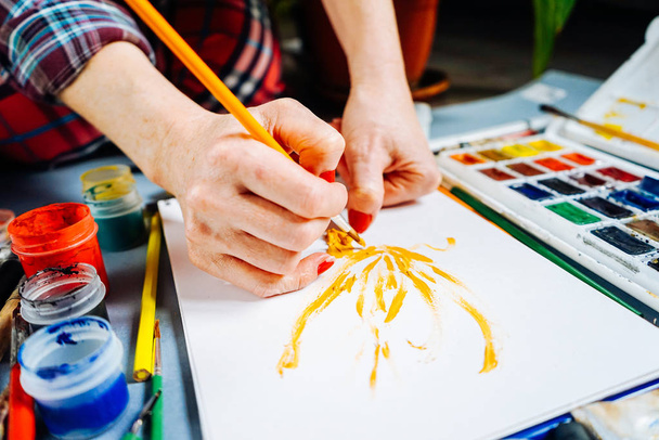 woman artist paints on white paper with bright watercolors - Fotó, kép