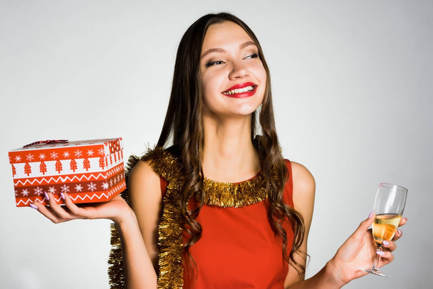 Gelukkig lachende meisje in de rode jurk vieren het nieuwe jaar, houdt van een glas champagne en een cadeau - Foto, afbeelding