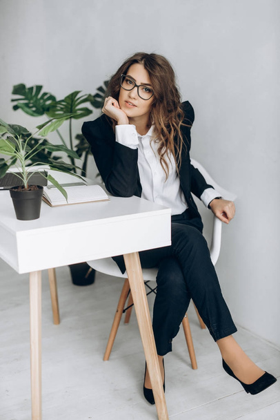 Femme d'affaires moderne dans un costume d'affaires et dans des lunettes est assis sur une chaise dans son élégant bureau lumineux
 - Photo, image