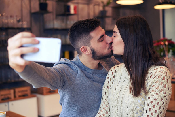 Couple making selfie while kissing at cafe - Photo, Image