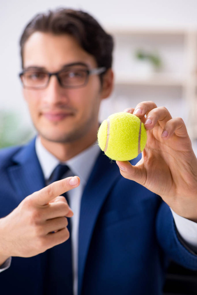 Молодий бізнесмен з тенісним м'ячем працює в офісі
 - Фото, зображення
