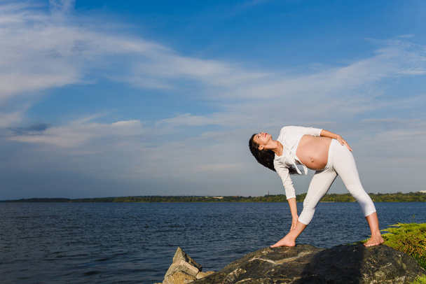 Mujer embarazada está practicando yoga junto al río
 - Foto, imagen