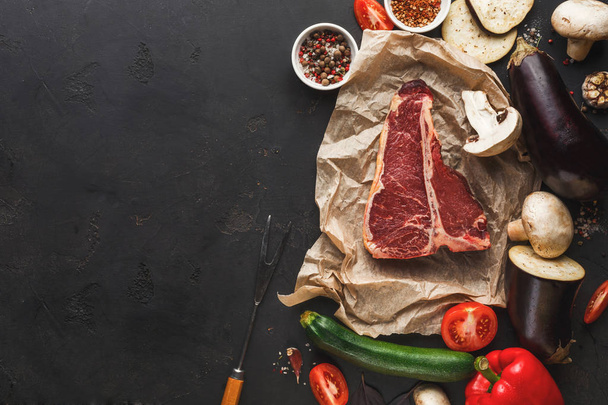 Raw t-bone steak on craft papper on dark background - Фото, изображение