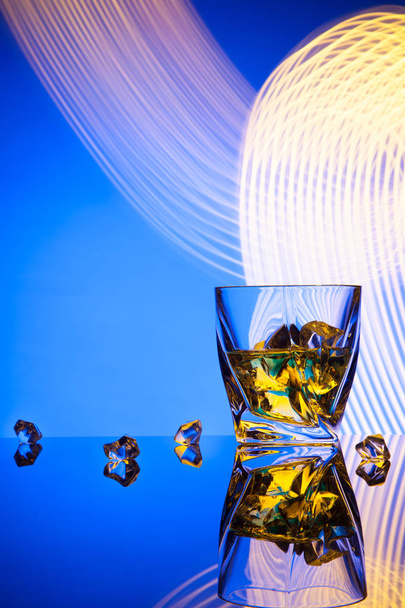 カクテル ウイスキー党青の背景に光の効果を概念の部分氷でガラス. - 写真・画像