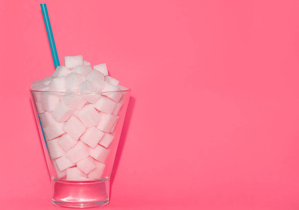 Glass with blue straw filled with sugar cubes on pink background. Junk food concept. - Fotoğraf, Görsel