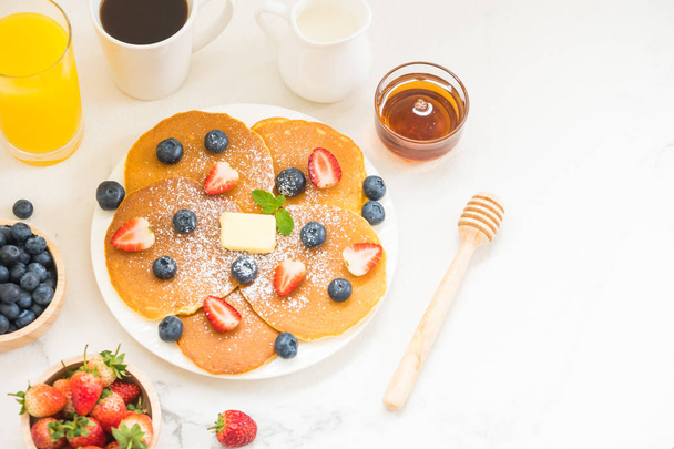 Egészséges reggeli szett palacsinta áfonya és eper gyümölcs és fekete kávé, tej és a narancslé a fehér kő asztal háttere - Fotó, kép