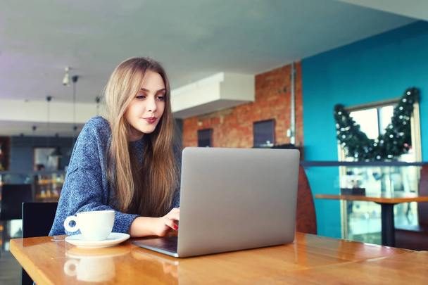 Woman working on laptop in a cafe. Young woman sitting at a table with a coffee usinglaptop. With blank copy space scree for your advertising text message or promotional content Toned image. Selective - Фото, зображення