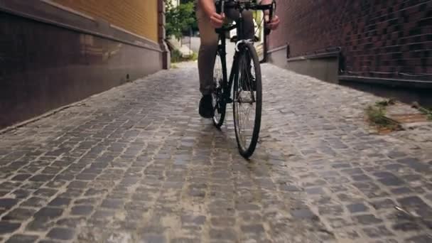 4k footage of stylish man riding black vintage bicycle om paved road of narrow street - Imágenes, Vídeo
