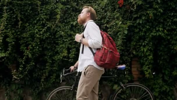 4k video of stylish young bearded man with bag walking with bicycle on street - Materiał filmowy, wideo