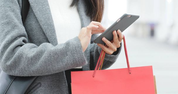 Κοντινό πλάνο Γυναίκα χρησιμοποιώντας το κινητό τηλέφωνο και κρατώντας τσάντες για ψώνια  - Φωτογραφία, εικόνα