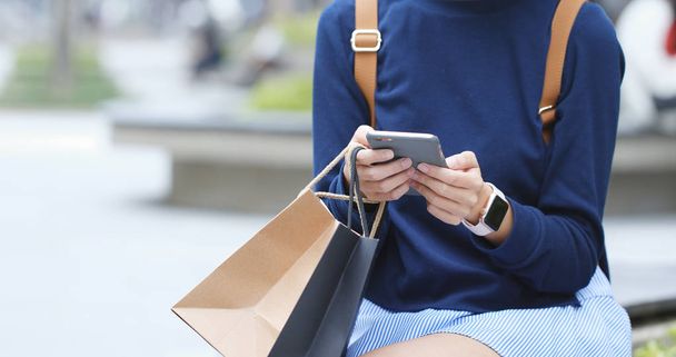 Frau benutzt Smartphone und hält Einkaufstüten in der Hand  - Foto, Bild