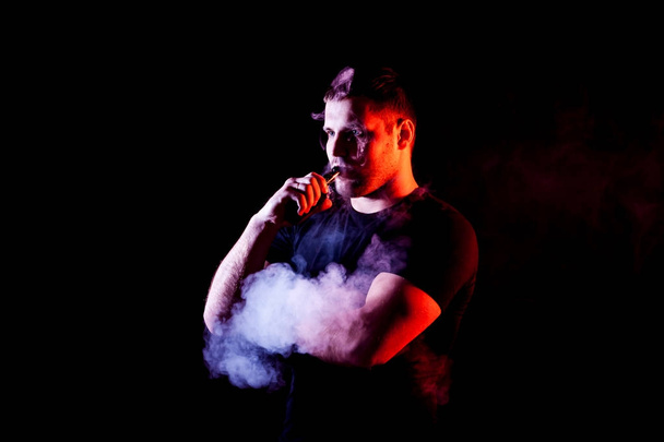 vaping man holding a mod. A cloud of vapor. Black background. - Фото, изображение