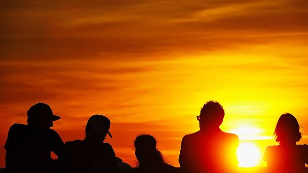 Силуэт людей наблюдает за закатом над закатом времени золотой фон неба
.                       - Фото, изображение