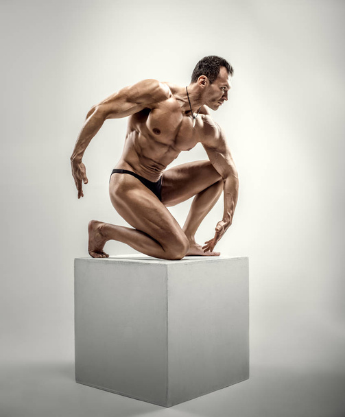 Very brawny athletic guy - bodybuilder,   pose on gray background - Фото, изображение