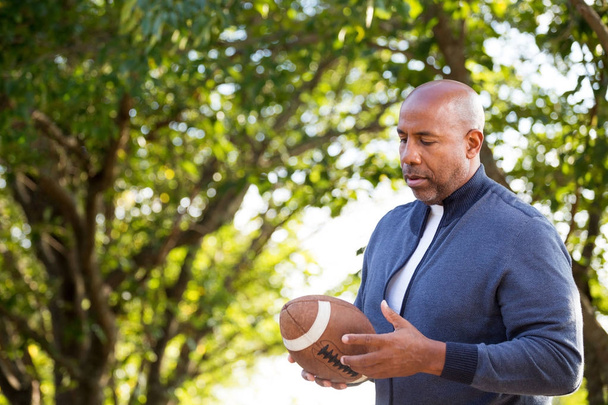 Mature African American man holding a football. - Фото, изображение