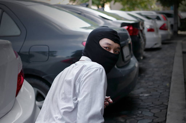 Masked burglar wearing a balaclava ready to burglary against car background. Insurance crime concept. - Photo, Image