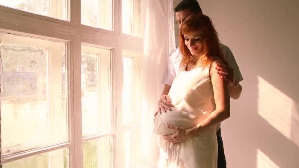 Kobieta w ciąży i jej mąż są stojący w pobliżu okna - Materiał filmowy, wideo