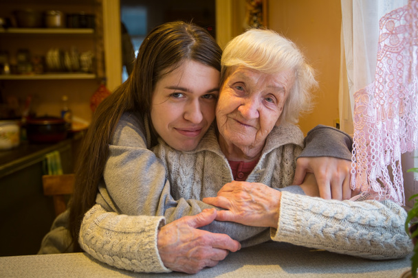 Una anciana en un abrazo con una nieta adulta posando para la cámara en una casa de pueblo
. - Foto, Imagen