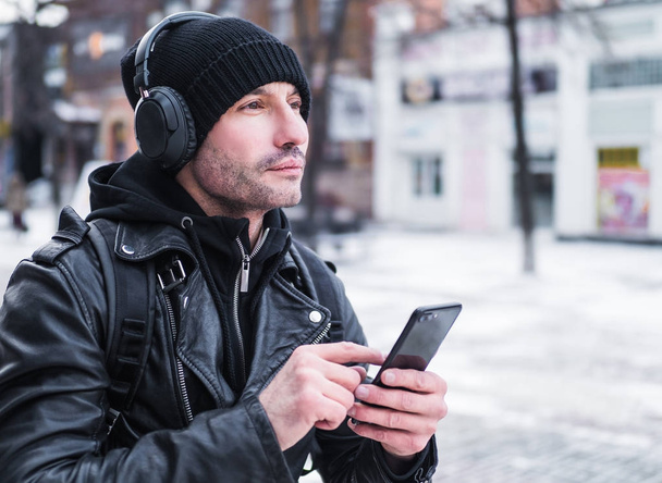Man looking for a place using GPS map in smartphone. He lost in unknown city. he is dressed in a leather jacket, hat and headphones - Photo, Image
