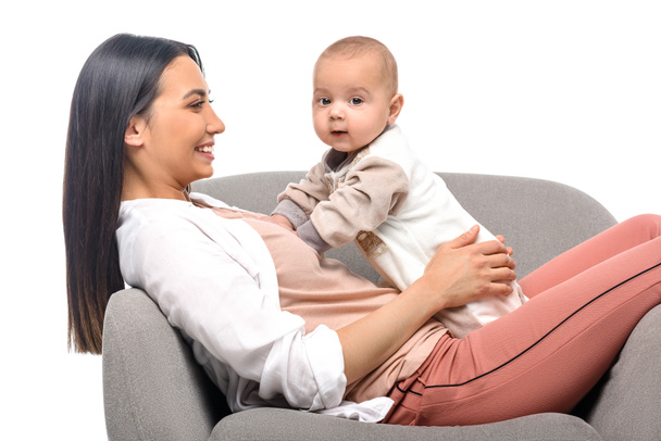souriant jeune mère reposant sur fauteuil avec petit bébé isolé sur blanc
 - Photo, image