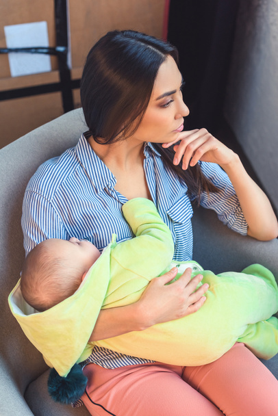 thoughtful mother with infant baby resting on arm chair at home - Foto, imagen