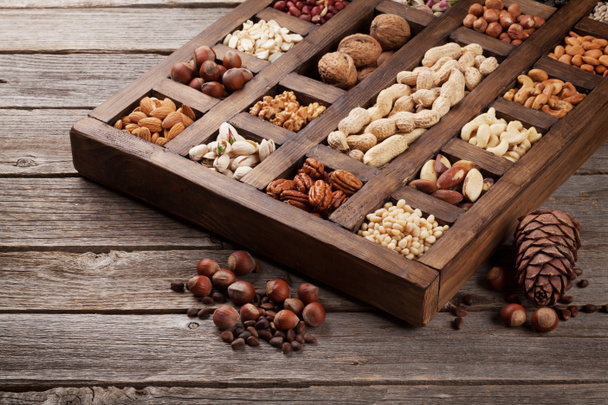 Разнообразный выбор орехов: арахис, фундук, каштан, грецкие орехи, фисташки и пеканы в деревянной коробке. Вид сверху
 - Фото, изображение