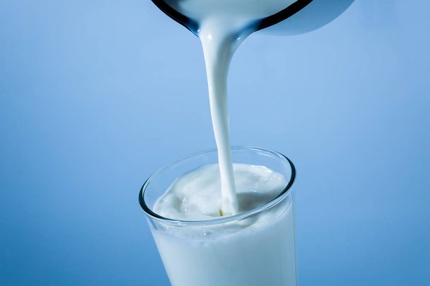 Milch aus der Blechdose in ein Glas auf blauem Hintergrund gießen - Foto, Bild